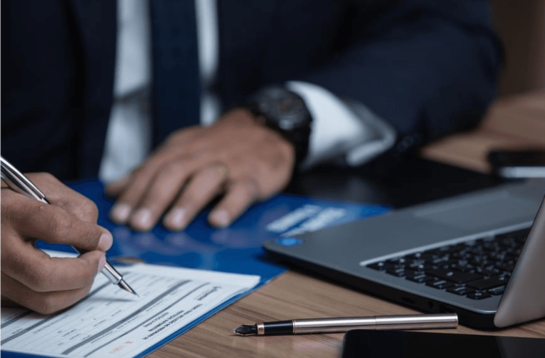 Professional hands writing on documents with laptop and pen